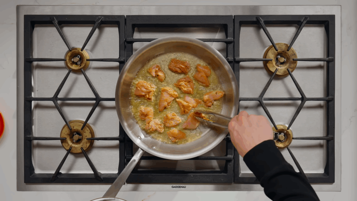 Butter chicken pieces cooking in oil in a skillet.