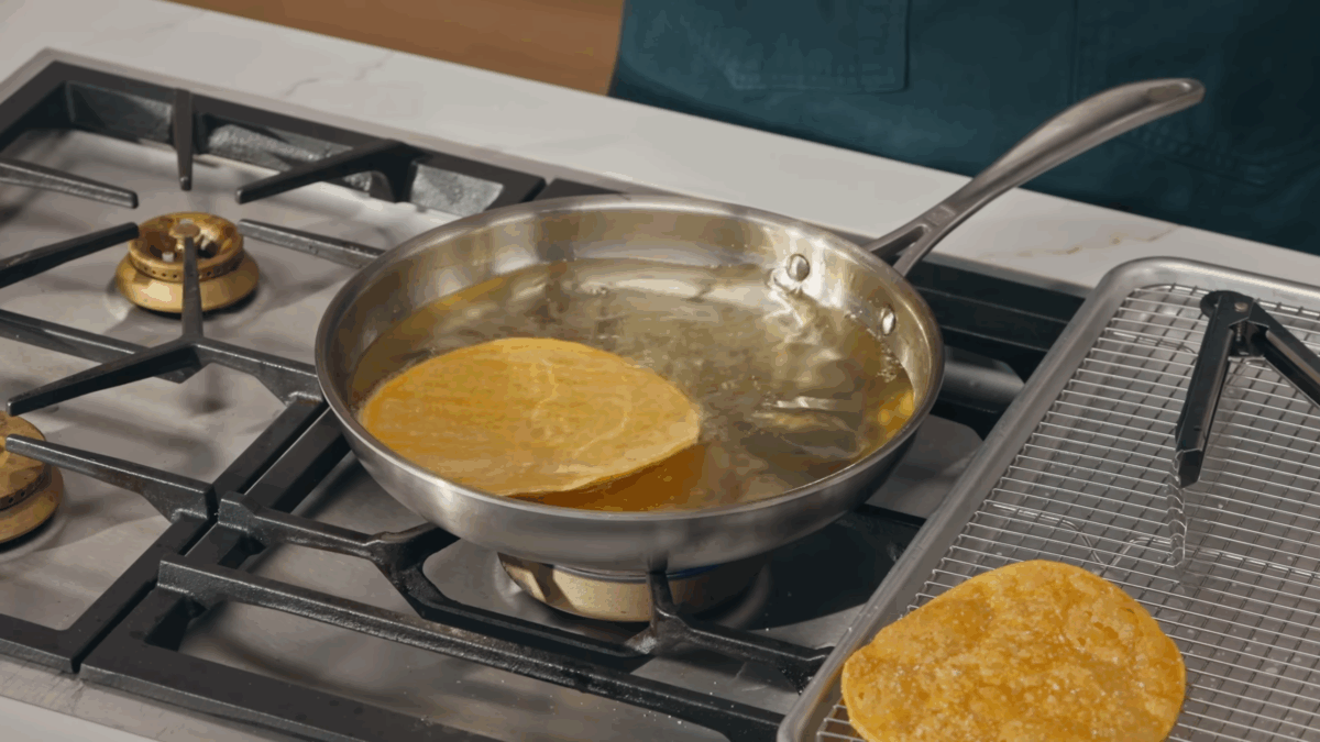 A tostada shell frying in oil in a skillet. 
