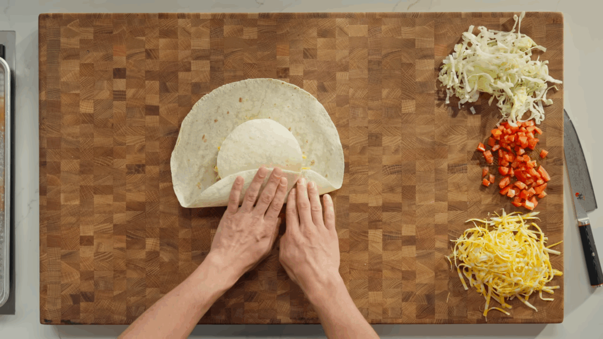 Two male hands folding a homemade crunchwrap supreme. 