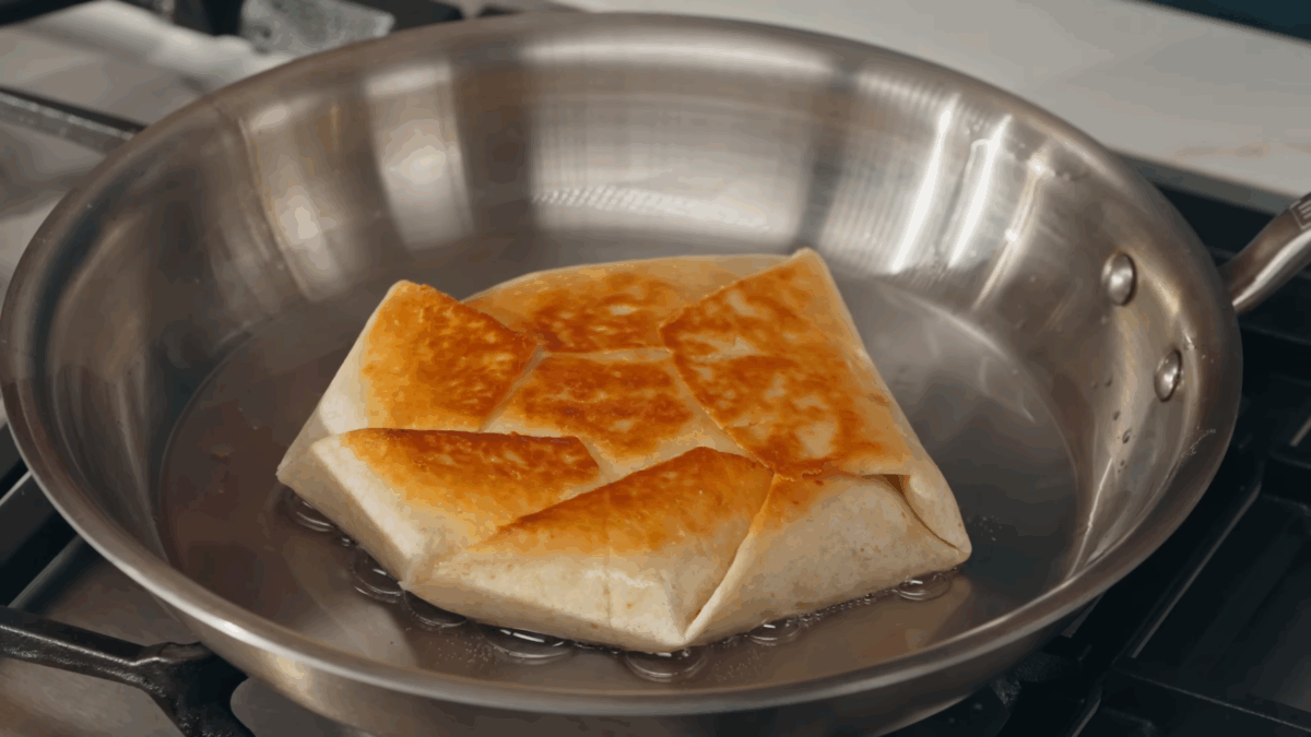 A homemade crunchwrap supreme cooking in a skillet. 