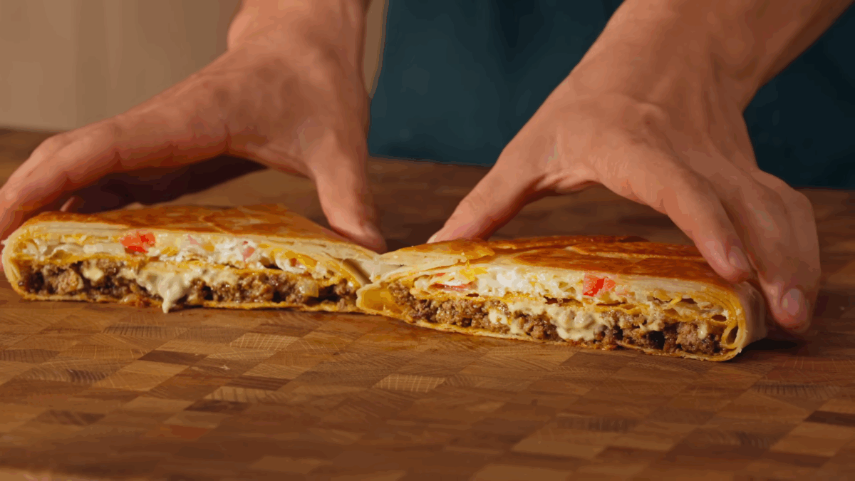Male hands pulling two halves of a homemade crunchwrap supreme apart. 