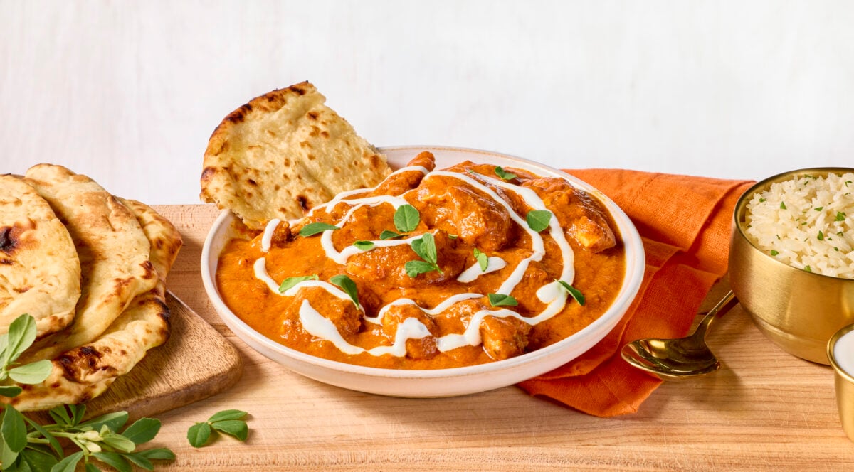 A bowl of butter chicken with a piece of naan bread sticking out.