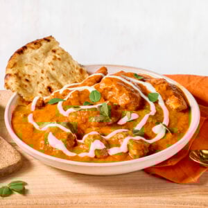A bowl of butter chicken with a piece of naan bread sticking out.