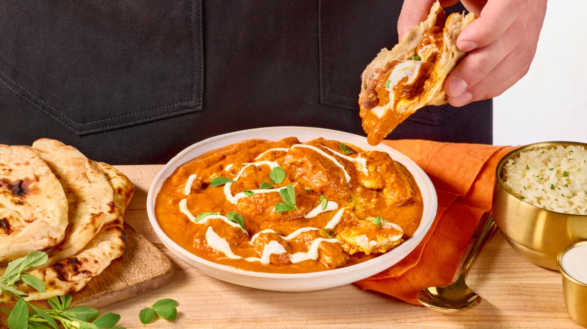Naan bread being dipped into a bowl of butter chicken.