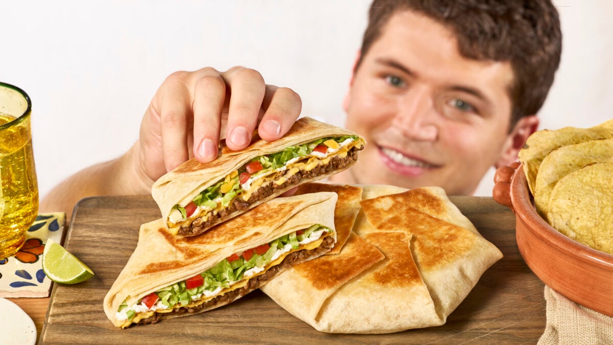 Nick DiGiovanni grabbing a crunchwrap supreme half from a cutting board. 