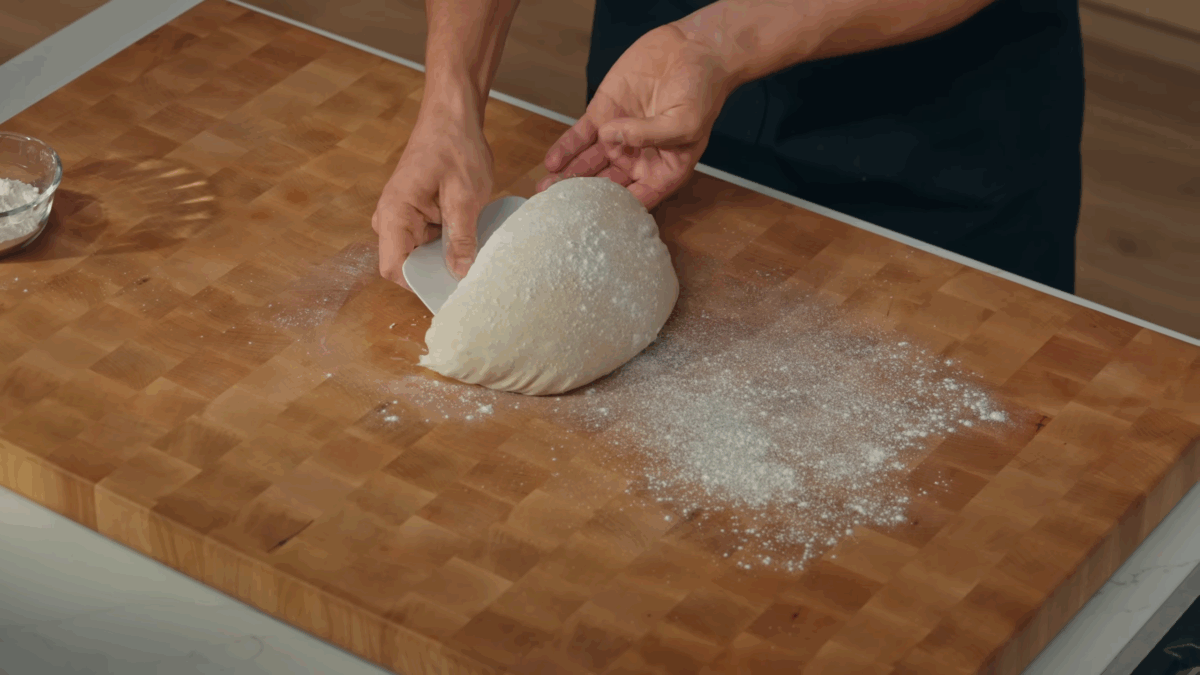 Nick DiGiovanni dragging sourdough bread dough on a floured work surface.