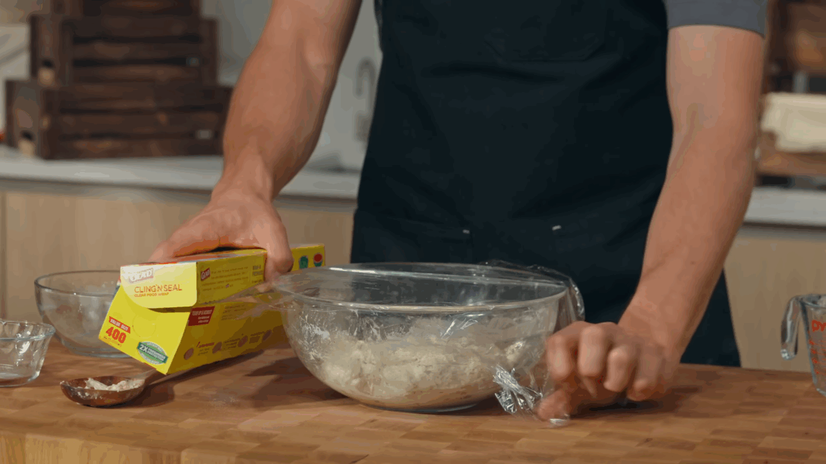 Nick DiGiovanni covering a bowl of sourdough bread dough with plastic wrap.