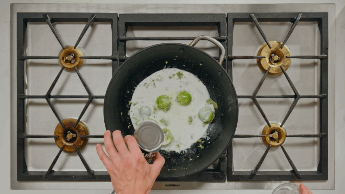 Coconut milk being poured into a skillet with coconut cream and Thai eggplant.