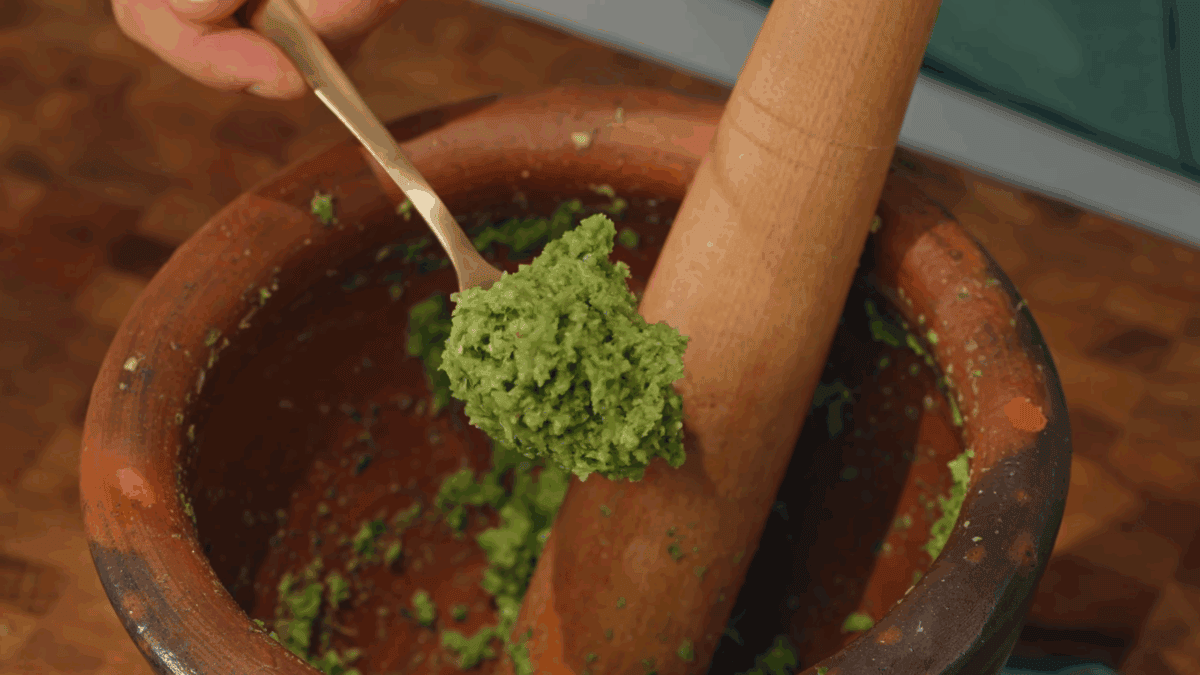 A spoon lifting a scoop of Thai green curry paste from a mortar and pestle.