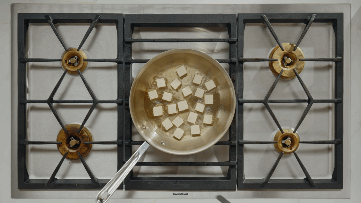 Pressed tofu cubes cooking in oil in a skillet on a stovetop.