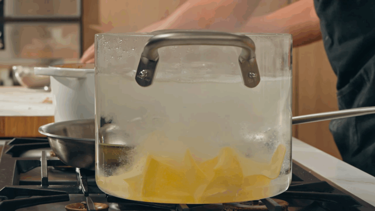 Homemade pappardelle noodles boiling in a pot of water on a stovetop.