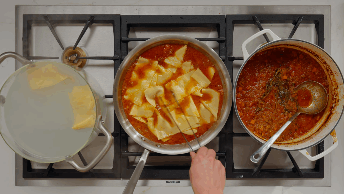 Freshly cooked pappardelle being added to a pan of bolognese sauce.