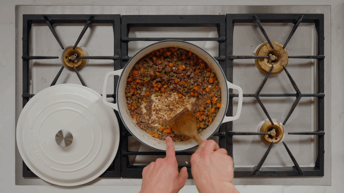 Nick DiGiovanni deglazing a Dutch oven of ground beef, ground pork, carrots, celery, and onions with white wine.