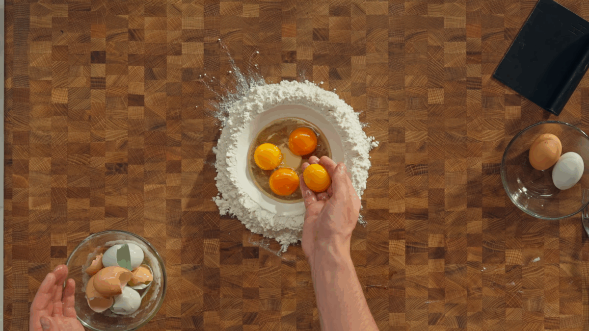 Nick DiGiovanni adding eggs to a well of flour on a wooden cutting board.