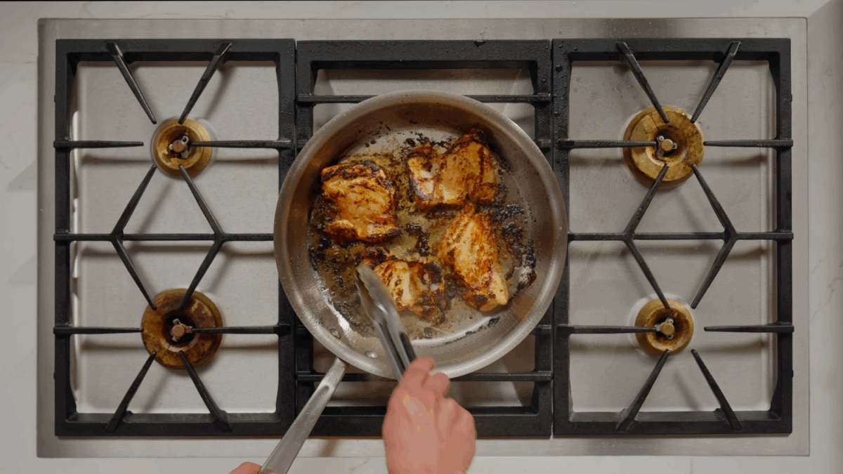 Nick DiGiovanni cooking four marinated chicken thighs in a skillet on the stove.