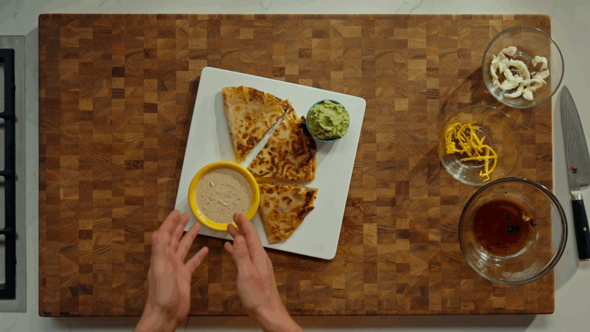 Three slices of a chicken quesadilla on a white plate with chipotle sauce and guacamole.