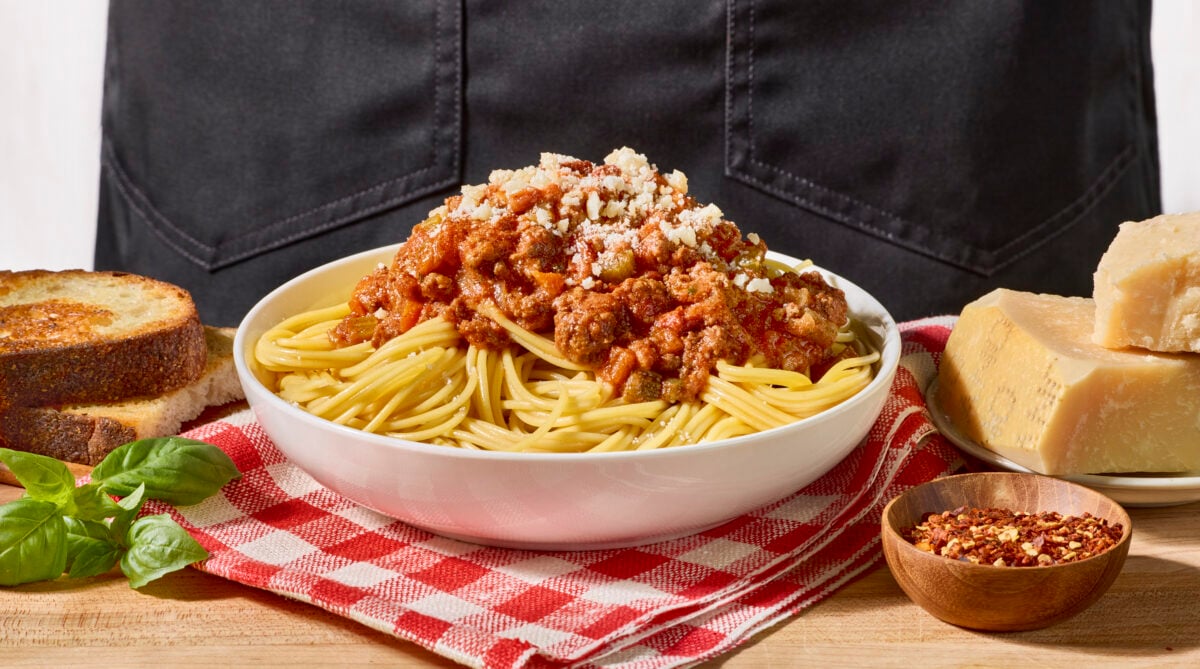 A bowl of spaghetti bolognese toped with Parmesan cheese.