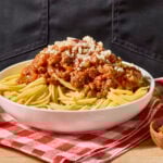 A bowl of spaghetti bolognese toped with Parmesan cheese.