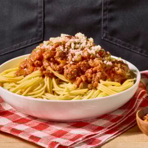 A bowl of spaghetti bolognese toped with Parmesan cheese.