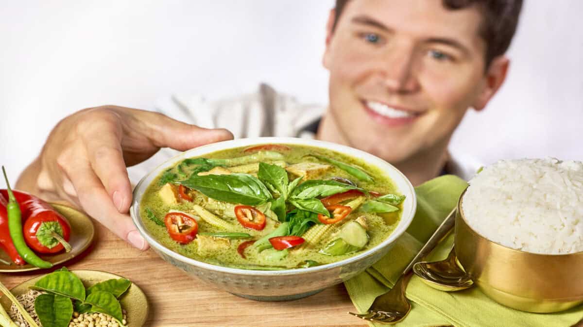 Nick DiGiovanni holding a bowl of Thai green curry next to plates of chiles, herbs, Jasmine rice, a spoon, and fork.