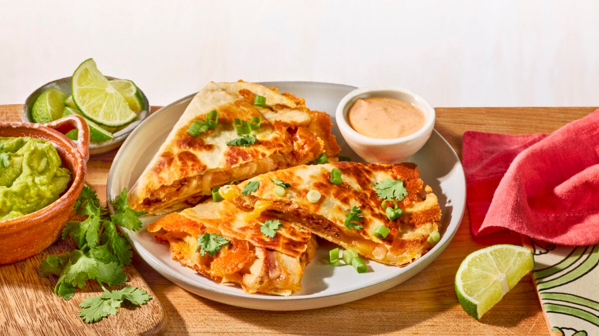 Three slices of a homemade chipotle chicken quesadilla on a white plate next to a bowl of chipotle sauce.
