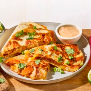Three slices of a homemade chipotle chicken quesadilla on a white plate next to a bowl of chipotle sauce.
