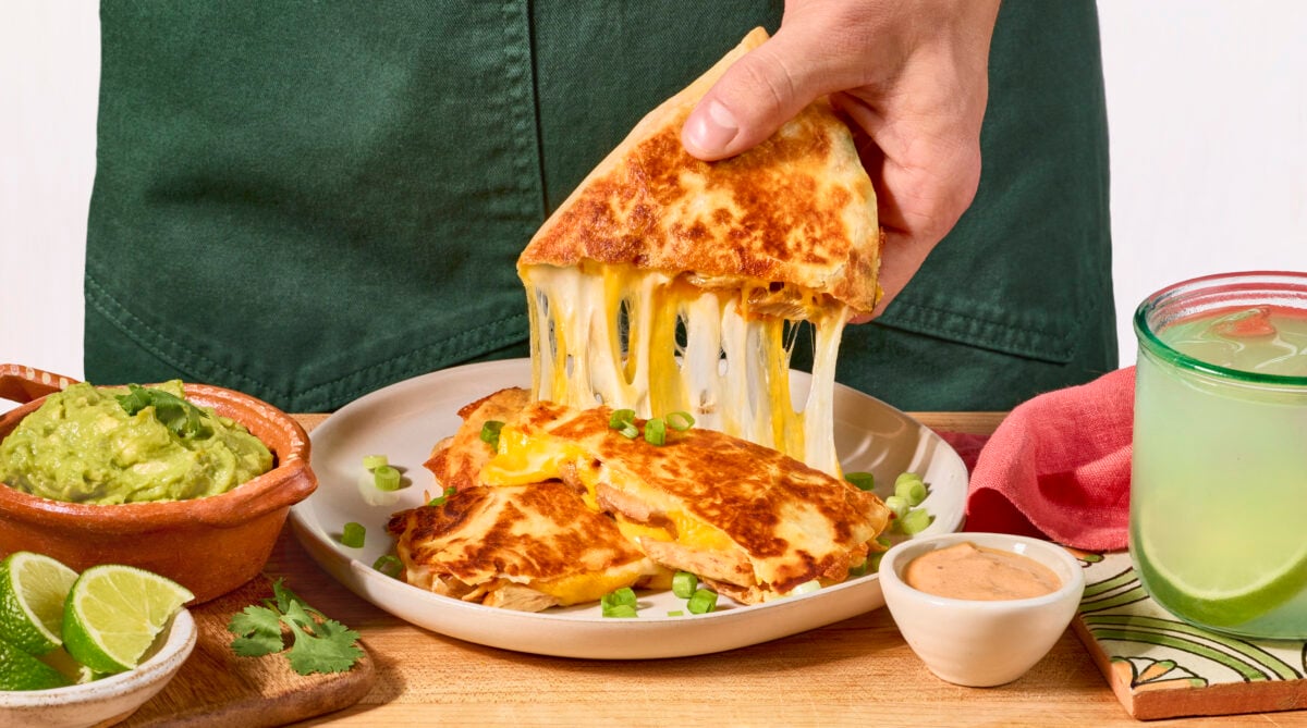 Nick DiGiovanni lifting a slice of a chipotle chicken quesadilla from a white plate.