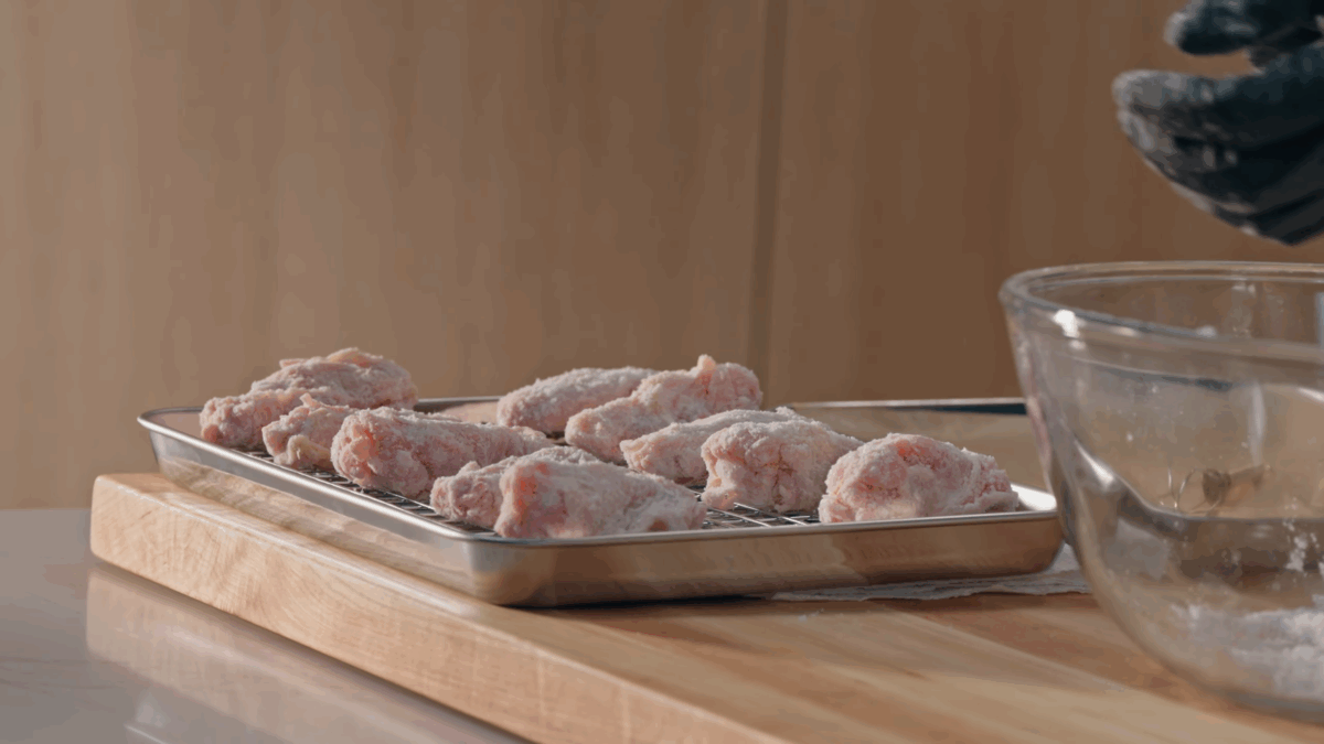 Raw breaded chicken wings on a sheet pan lined with a wire rack.