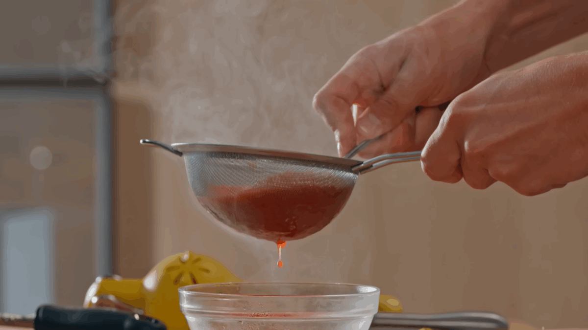 Nick DiGiovanni straining raspberry coulis through a fine mesh sieve.