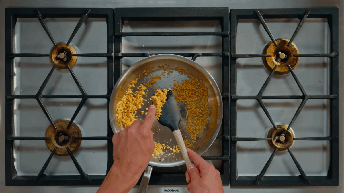 Breadcrumbs toasting in oil in a skillet on the stovetop.