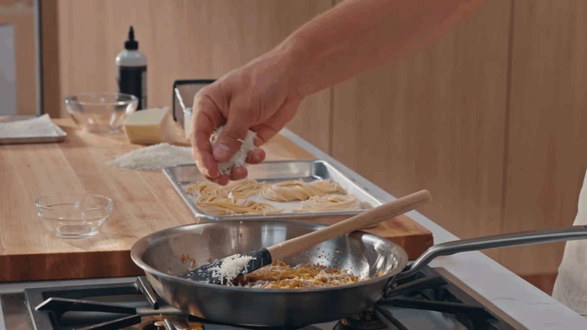 Pecorino being added to a skillet of pangrattato. 