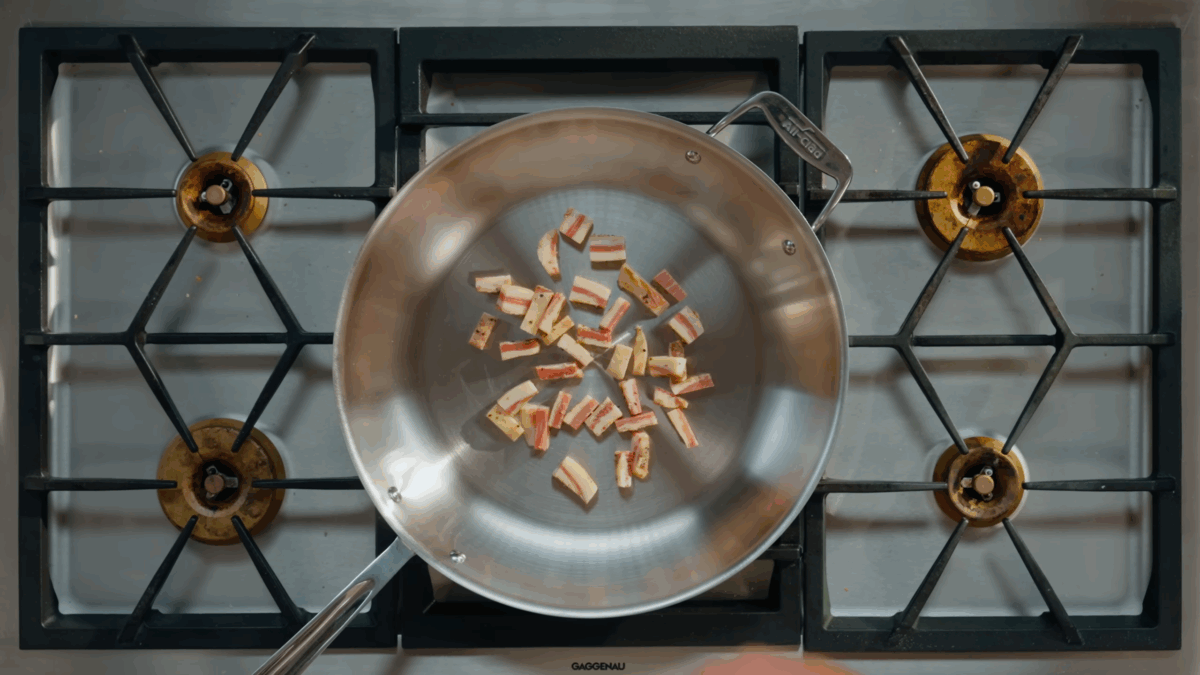 Guanciale pieces cooking in a skillet.