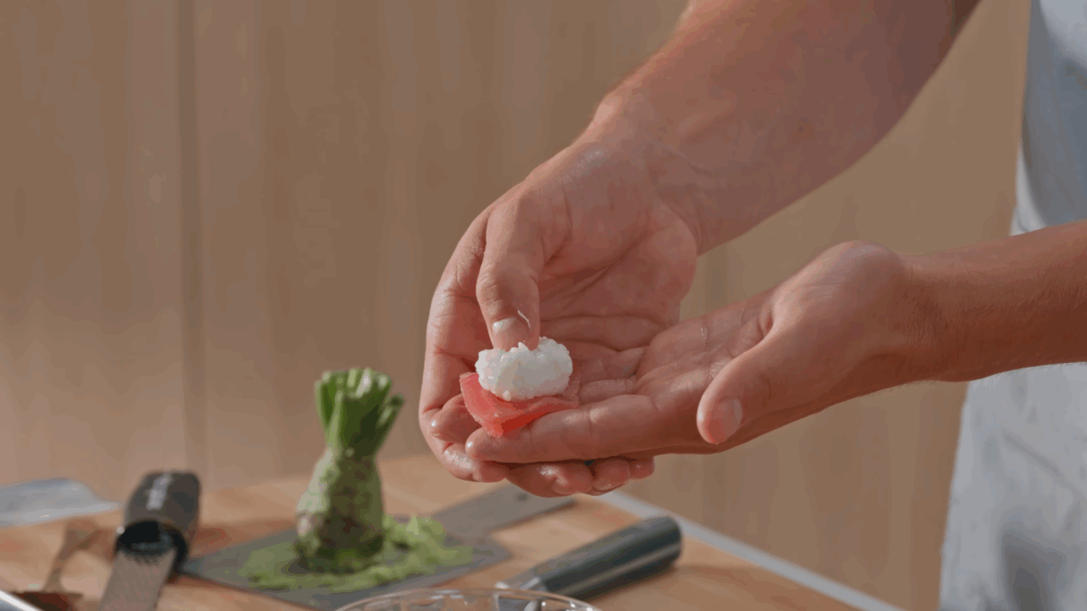 Rice, wasabi paste, and fish being layered for nigiri.