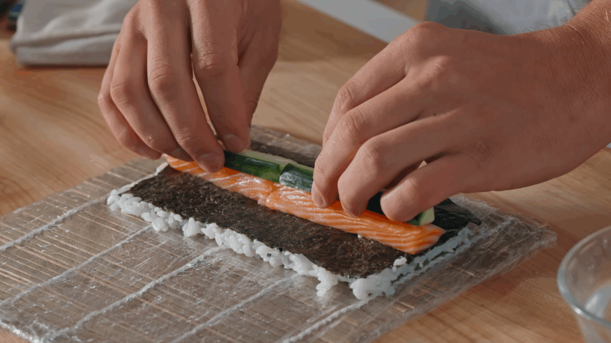 Nick DiGiovanni layering salmon and cucumber slices on a sheet of nori covered with sushi rice.