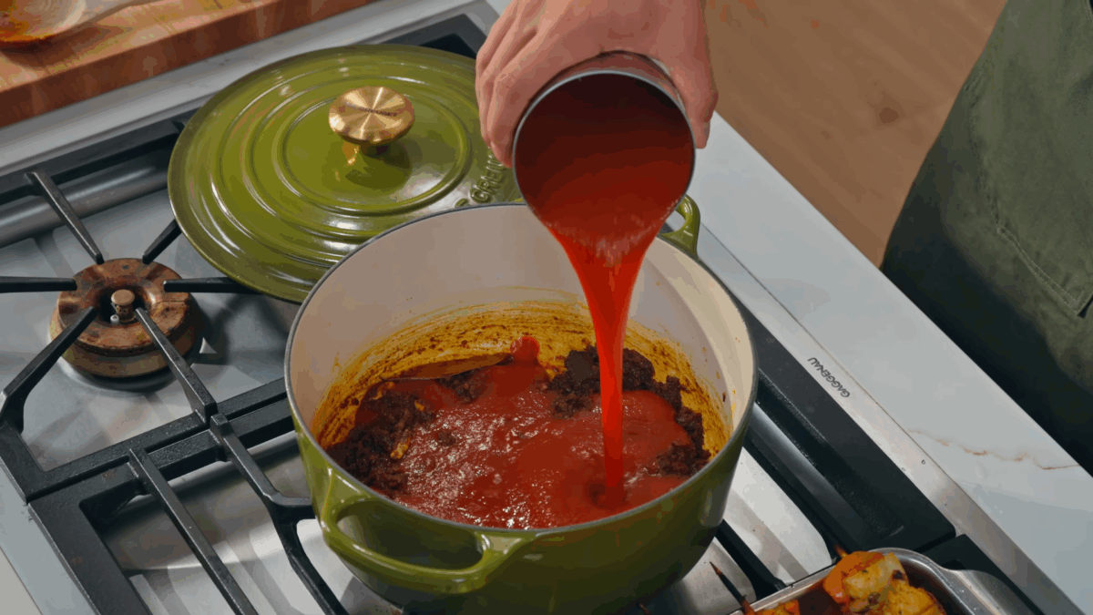Nick DiGiovanni pouring tomatoes into a Dutch oven.