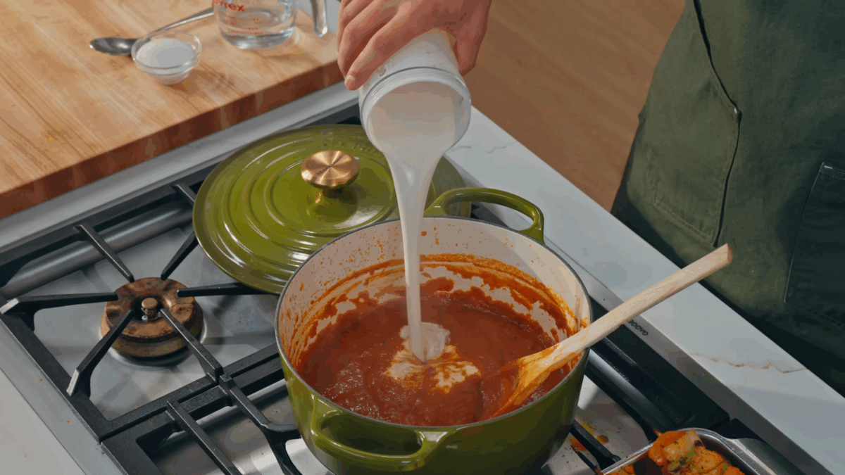 Nick DiGiovanni pouring cashew cream sauce into a pot of chicken tikka masala.