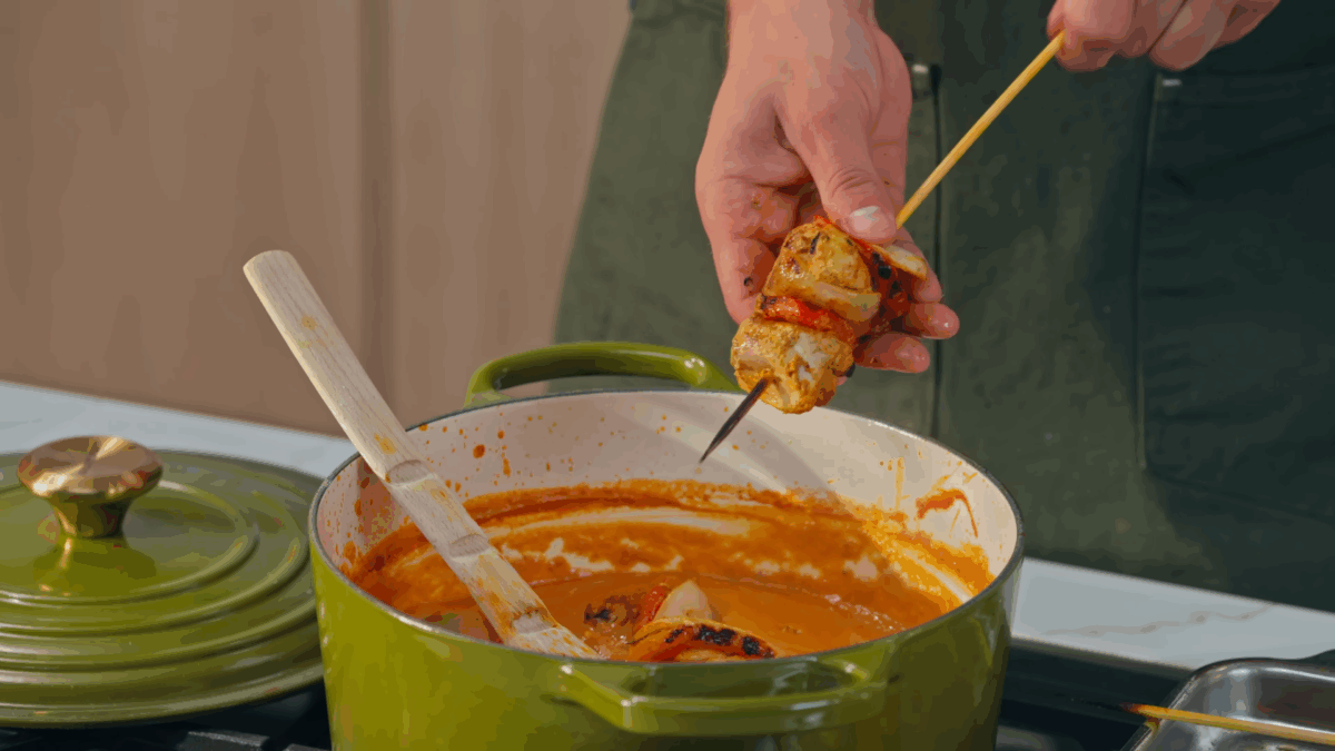 Nick DiGiovanni adding seared chicken, onions, and peppers to a pot of chicken tikka masala.