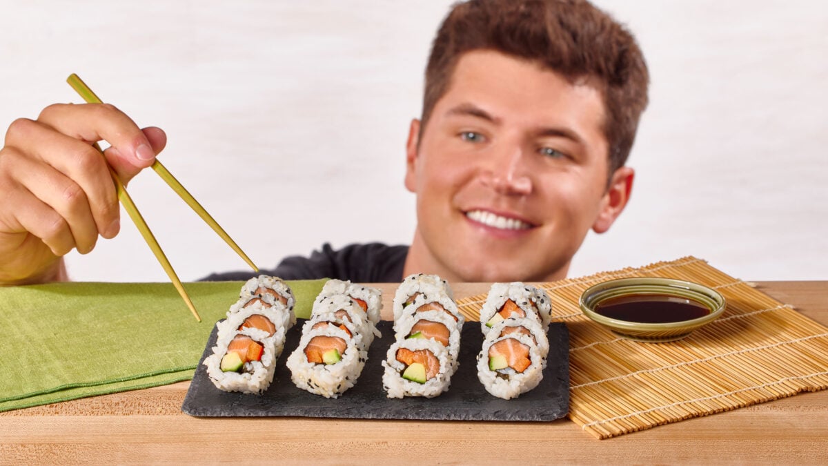 Nick DiGiovanni using chopsticks to grab a piece of sushi from a platter of homemade rolls.