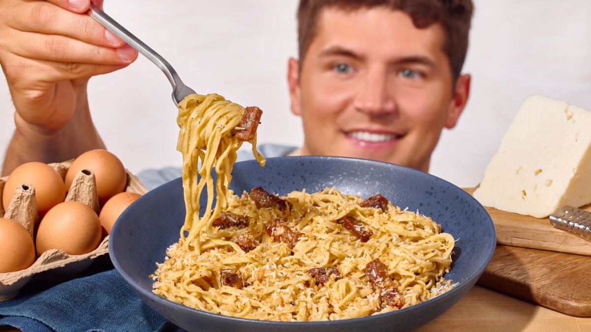 Nick DiGiovanni lifting a forkful of pasta carbonara from a blue bowl. 