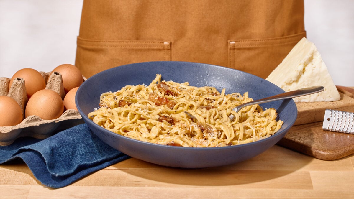 A bowl of pasta carbonara topped with pecorino, a fork sticking out. 