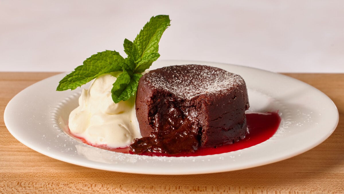 A molten chocolate lava cake on a plate with raspberry coulis, whipped cream, and a mint leaf, a bite missing from the cake.