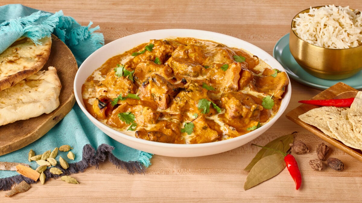 A bowl of chicken tikka masala next to basmati rice, naan, and pappadum.
