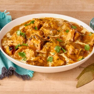A bowl of chicken tikka masala next to basmati rice, naan, and pappadum.