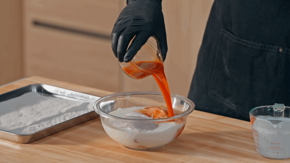 Raw chicken being combined with buttermilk and hot sauce in a bowl. 