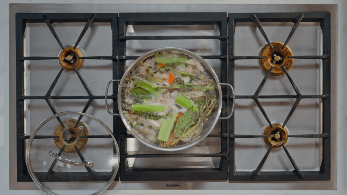 Beef stock ingredients simmering in a stock pot on the stovetop. 