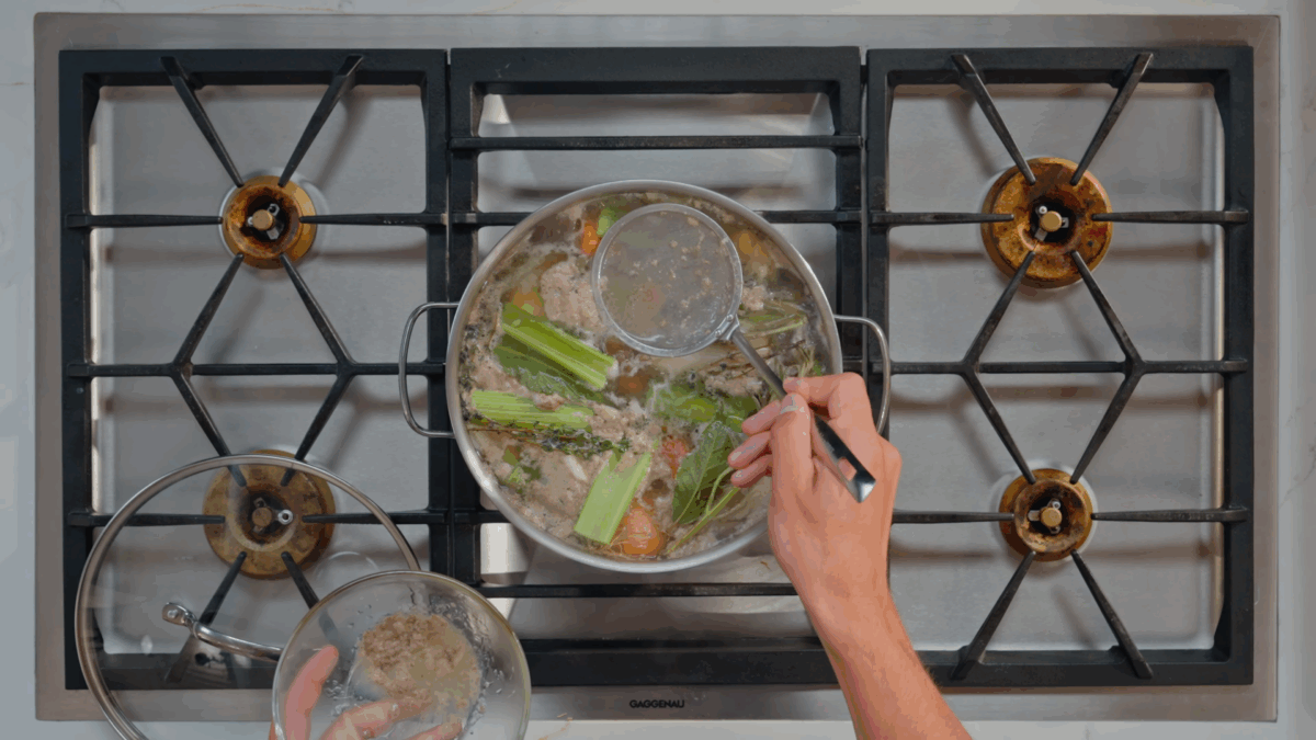Nick DiGiovanni straining fat from the top of a pot of simmering beef stock. 