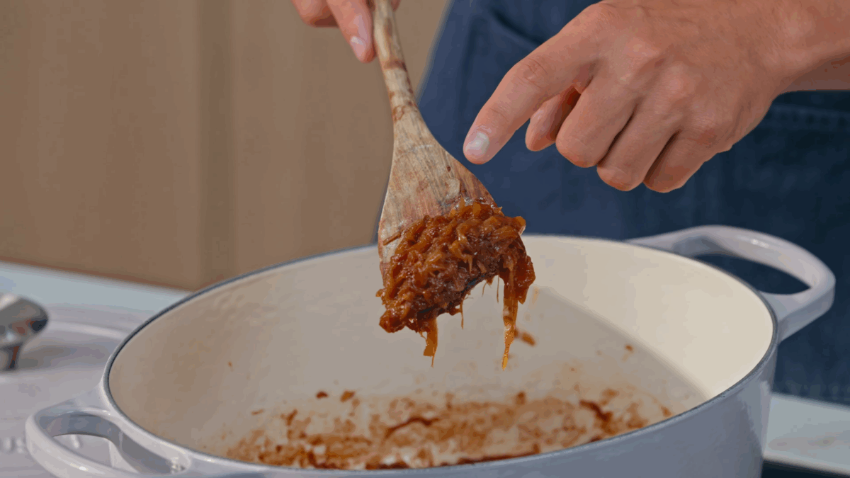 Nick DiGiovanni lifting a scoop of caramelized onions from a Dutch oven.