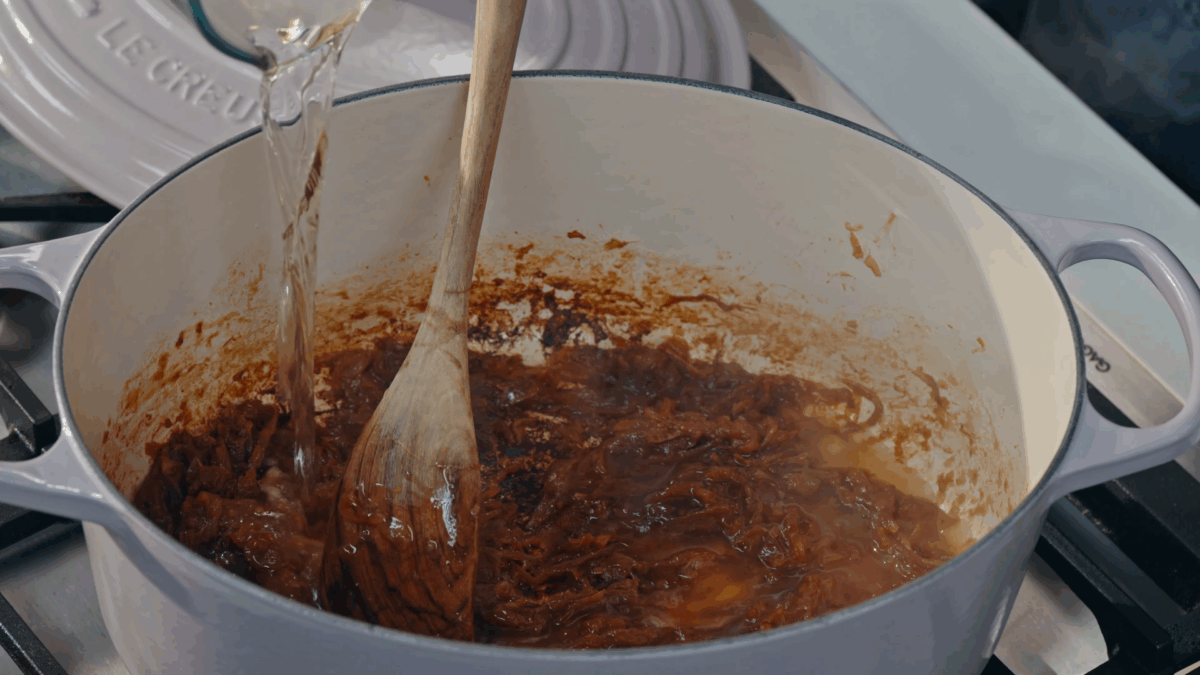 Nick DiGiovanni pouring white wine into a Dutch oven full of caramelized onions. 