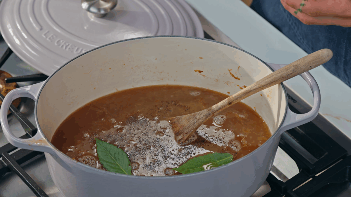 French onion soup in a Dutch oven topped with salt, pepper, and fresh herbs. 