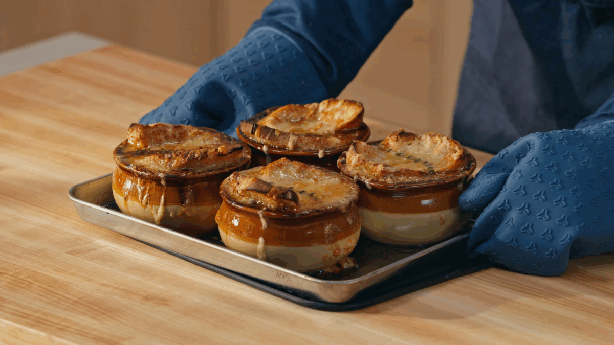 Nick DiGiovanni holding a baking sheet with four bowls of broiled French onion soup. 